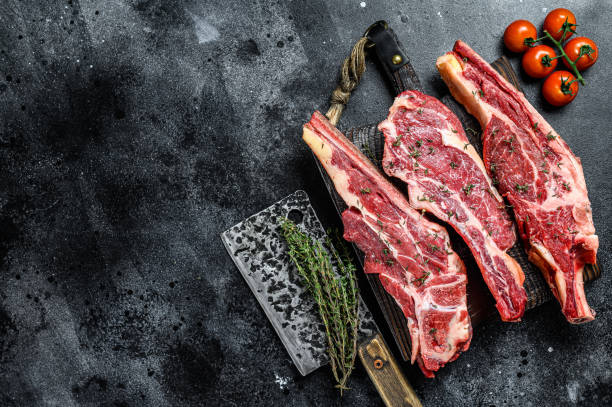istock Assortment of raw cuts beef meat steaks on the bone. Black background. Top view. Copy space 1298879237