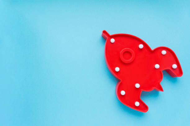 istock Red rocket ship lamp on blue background. Cosmonautics Day concept. Top view, copy space. 1298889670