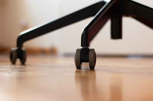 Black metal office chair lags with swivel wheels on wood floor tiling shallow depth of field nobody.