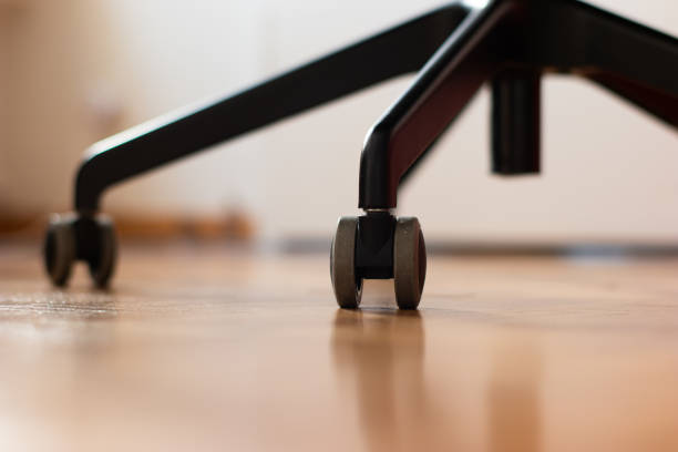 Black metal office chair lags with swivel wheels on wood floor tiling shallow depth of field nobody stock photo