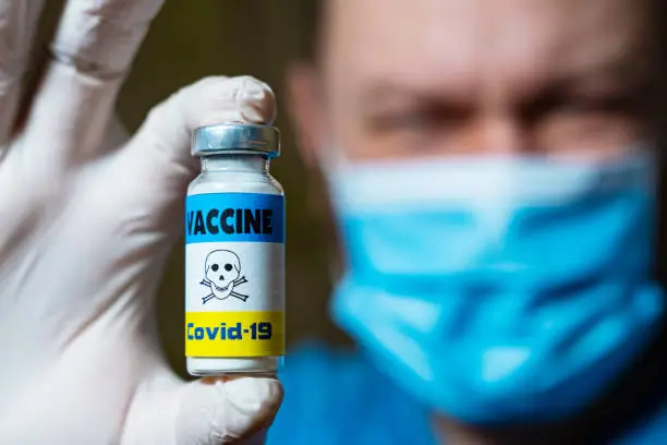 The dangers of coronavirus vaccination. Harmful side effects concept. Doctor holds a vial of vaccine with a toxicity warning sign.