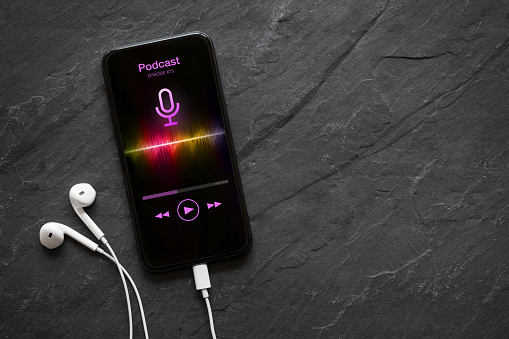 Earphones and mobile phone with podcast app on screen on black background