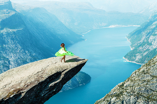 a girl in a light green dress dances on the trolltunga in Norway