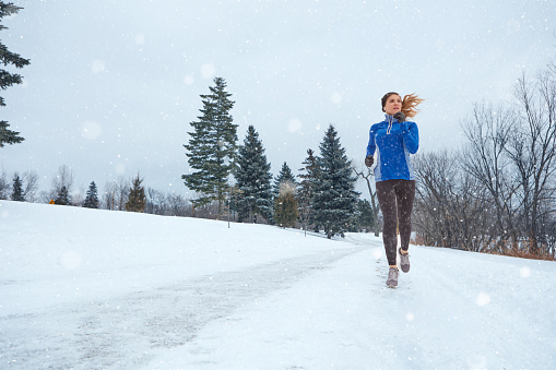 Shot of a woman wearing warm clothing while out for a run through the snow
