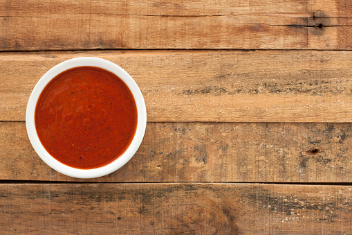 Top view of white bowl full of red hot sauce over wooden table