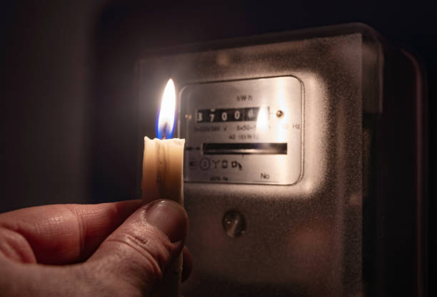 istock A persons's hand with candle in complete darkness looking on electricity meter at home. Power outage, blackout concept. 1298915738