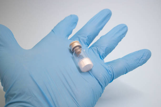 Doctor drawing up Covid-19 vaccine from glass phial bottle and filling syringe injection for vaccination. Close up of hand wearing protective disposable gloves in lab and holding a bottle of vaccination drugs. Hand with blue surgical gloves taking sars-coV-2 vaccine dose from vial with syringe: prevention and immunization concept.