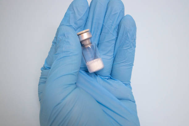 Doctor drawing up Covid-19 vaccine from glass phial bottle and filling syringe injection for vaccination. Close up of hand wearing protective disposable gloves in lab and holding a bottle of vaccination drugs. Hand with blue surgical gloves taking sars-coV-2 vaccine dose from vial with syringe: prevention and immunization concept.