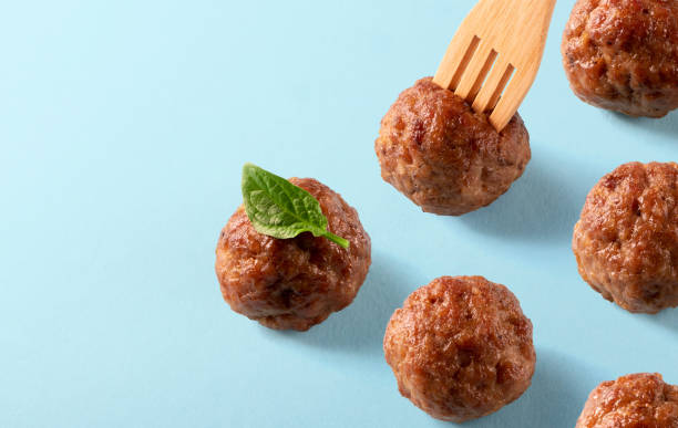 Italian cuisine beef meatballs with basil leaf and wooden fork on blue background. Template for menu, recipe or packing. Delicious food, isometric stock photo