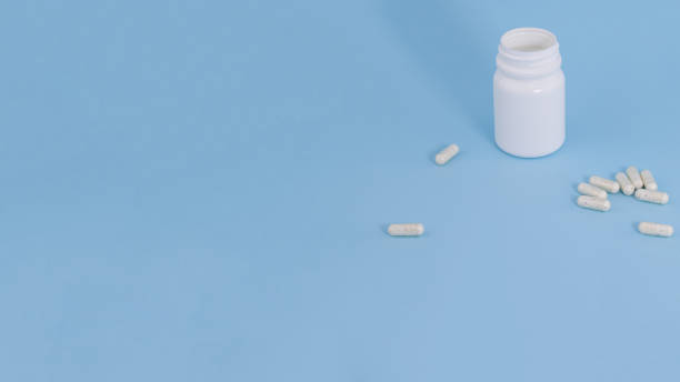 istock bottle with scattered pills on blue background with copy space 1298920988