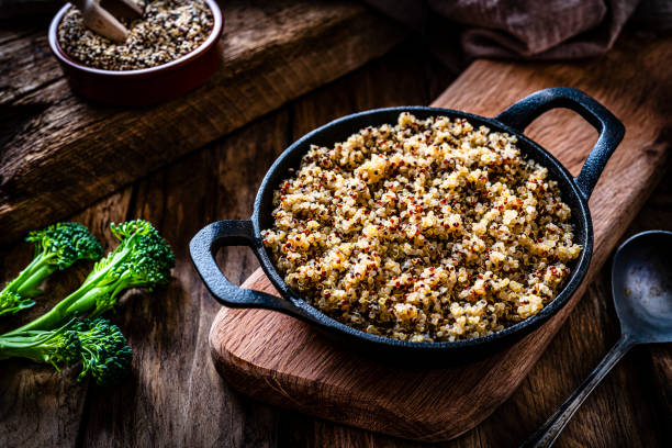 Cooked quinoa in a cast iron pan on rustic wooden table. Vegan food: cooked quinoa in a cast iron pan shot on rustic wooden table. Predominant colors are brown and green. High resolution 42Mp studio digital capture taken with SONY A7rII and Zeiss Batis 40mm F2.0 CF lens quinoa photos stock pictures, royalty-free photos & images