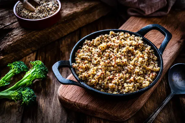 Photo of Cooked quinoa in a cast iron pan on rustic wooden table.