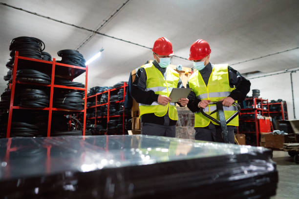 istock Two young warehouse workers with protective face mask sorting finished rubber mats for gym in warehouse by using digital tablet and pallet jack 1298924628