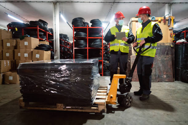 istock Warehouse workers with protective face mask sorting finished rubber mats for gym in warehouse by using digital tablet and pallet jack 1298924646