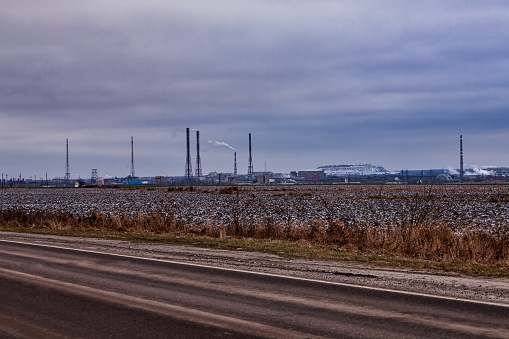 Industrial landscape in late autumn. Smoking chimneys of an industrial plant, snow-dusted fields under a cloudy autumn sky