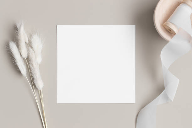 istock Square invitation card mockup with a lagurus on a beige table. 1298926789
