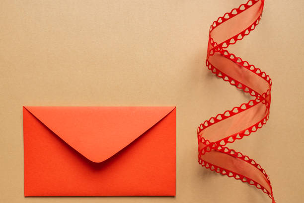 istock Valentine's day or Wedding romantic concept. Twisted decorative ribbon and red envelope with red hearts on beige background. 1298932520