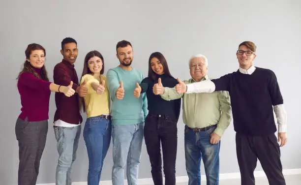 Photo of Group of happy diverse people standing together, giving thumbs-up and looking at camera