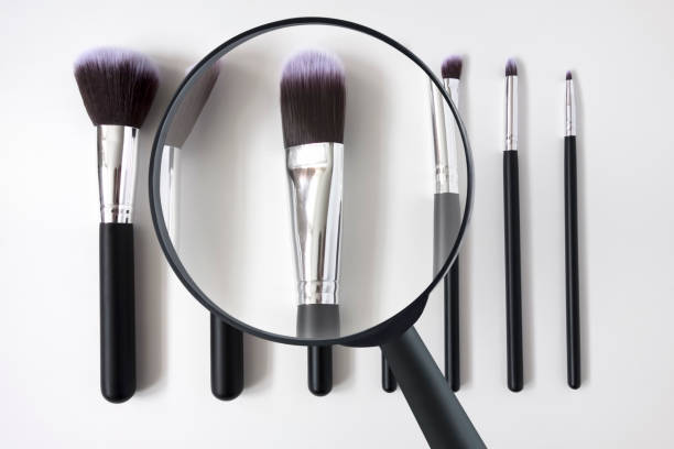 looking down on magnifying glass and make up brushes on a white background