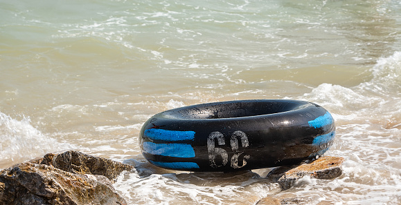 Close up of black inflatable ring or rubber ring on the rock in sea beach. dirty swimming ring with sand on sea waves, nobody on the beach, nature concept
