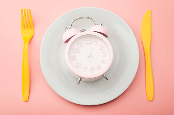 istock Weight loss strategy metaphor and intermittent fasting plan concept with minimal photography of clock on empty plate and vibrant yellow fork and knife isolated on vivid pink background 1298941668