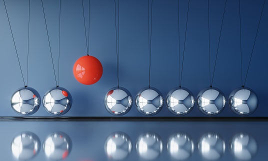 A red colored hanging sphere standing out from the chrome ones in pendulum. ( 3d render )