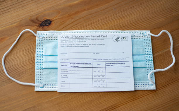 Covid-19 Vaccination Record card by CDC covered blue  medical mask. stock photo