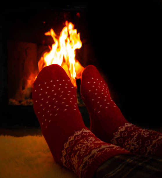 istock Female feet in red woolen socks by a warm fireplace on a cold winters evening. Shallow depth of field. 1298945340