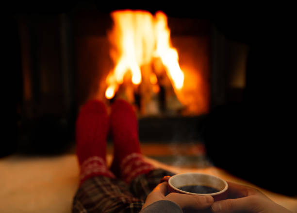istock Hands holding a steaming warm cup of coffee while resting by a fireplace on a cold winters evening. 1298945382