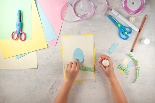 istock DIY and kids creativity. Step by step instruction: how to make card Happy easter. Step2 glue paper grass and egg rabbit torso . Childrens handmade Easter craft 1298947150
