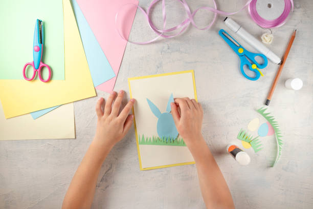 DIY and kids creativity. Step by step instruction: how to make card Happy easter. Step3 glue paper ears of rabbit. Childrens handmade Easter craft stock photo