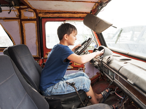 An 11-year-old boy plays as a driver behind the wheel of an old abandoned car.