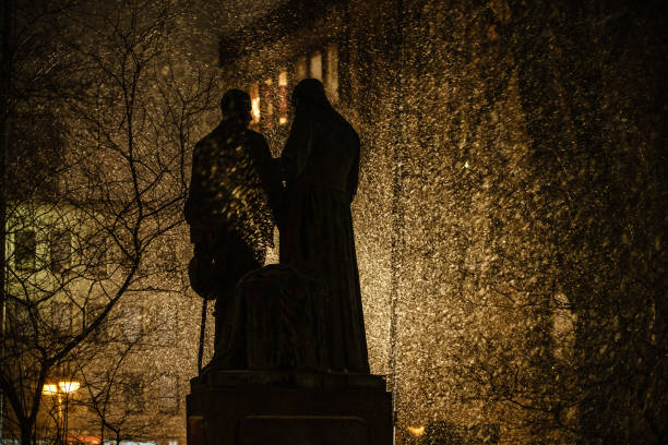 Cologne - Germany, January 22 2019: The photo shows the statue of Adolph Kolping in Cologne in winter. Snow is driving all around and a street light behind the statue casts its rays through the holes in the statue, making rays of snow visible