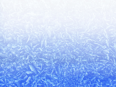 A close-up directly above a surface of frozen snowflake ice crystals in a cold Winter weather environment, with a color gradient from bright white at the top to blue at the bottom.