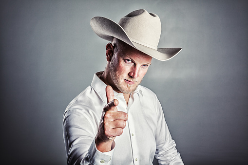 Studio portrait of a man wearing a white cowboy hat, pointing his finger gun at the camera