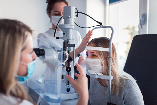 Young woman wearing a medical protective mask when having eye pressure measured at the ophthalmologist