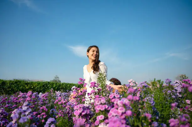 Photo of Young asian woman in white dress enjoying margaret flower blooming in garden