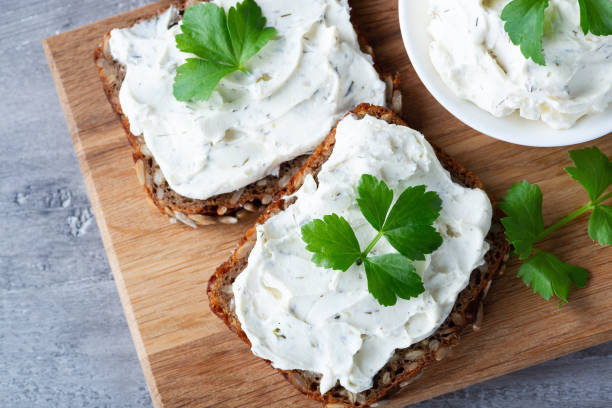 Home made bread on a wooden cutting board with curd cheese and ricotta and herbs. Decorated with green herbs Home made bread on a wooden cutting board with curd cheese and ricotta and herbs. Decorated with green herbs cream cheese photos stock pictures, royalty-free photos & images