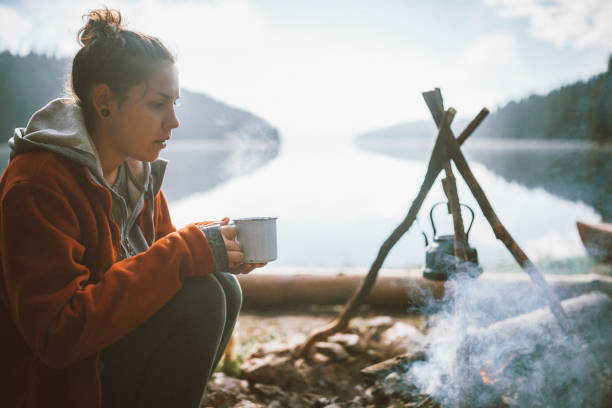istock Young Beautiful Female Is Sitting And Drinking Hot Tea Next To The Camp Fire 1298959018