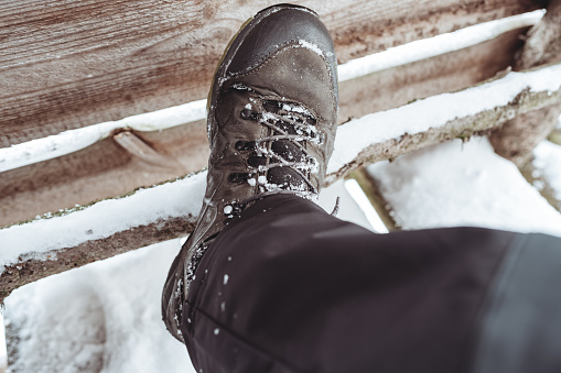 A resting hiker leaning his trekking boot on a wooden platform covered with snow on a winter day.