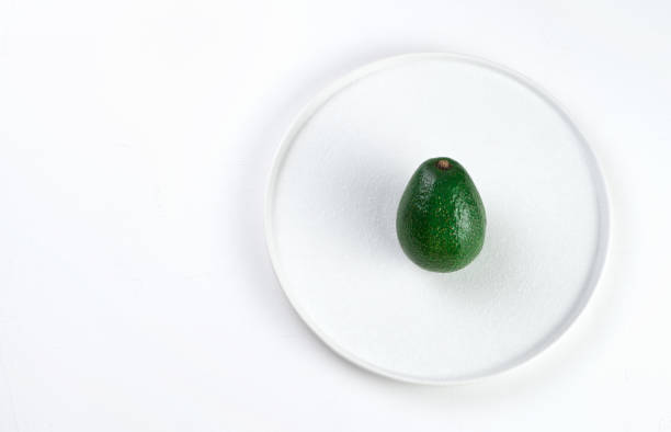 Green unpeeled avocado in a flat white plate on a light background