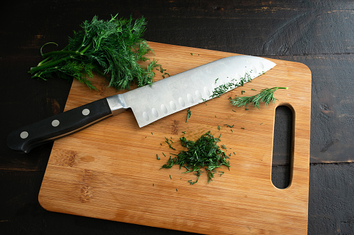 Finely chopping an organic seedless cucumber on a bamboo cutting board