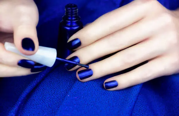 Photo of Female fingers with blue manicure hold a bottle of blue nail polish.
