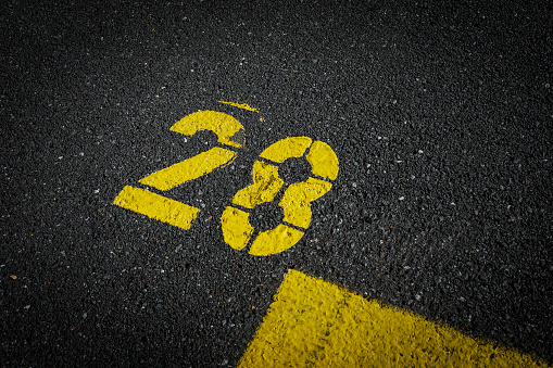 sign on the asphalt, yellow painted number twenty eight on grey street, yellow lines like a corner on the road, space for text