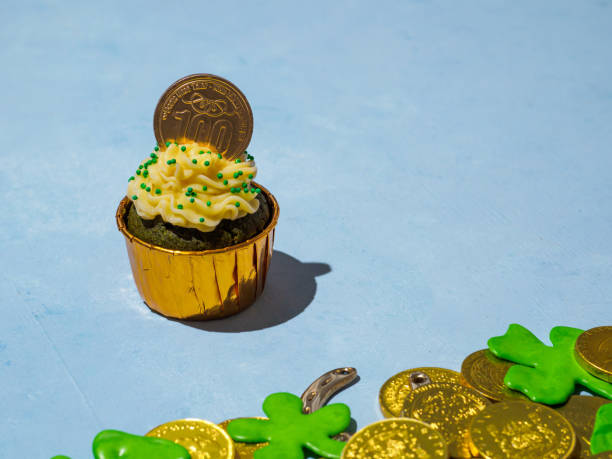 Saint Patricks day decoration on paper background. Golden coins, cupcakes, shamrocks made of sugarpowder. Copy space for text.