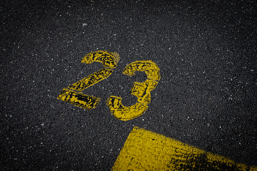 sign on the asphalt, yellow painted number twenty three on grey street, yellow lines like a corner on the road, space for text