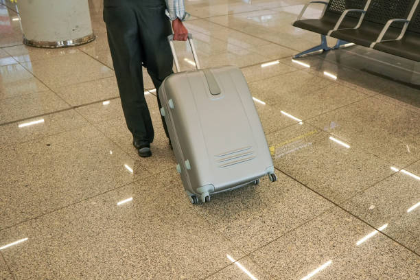 istock Man pulling his trolley baggage behind him at airport, view from back, only legs and luggage on floor visible 1298979829