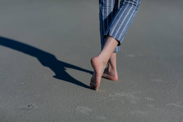 istock Woman's feet walking away on a sandy beach with back toes pointed. 1298980062