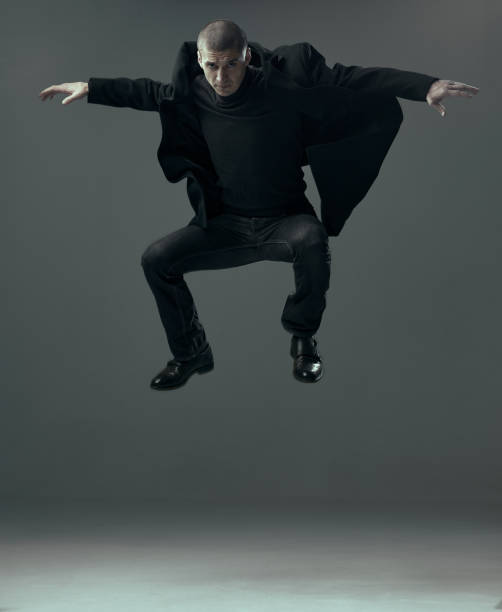 コピースペースを持つ灰色のスタジオの背景に浮上黒い服のビジネスマンでクールなハンサムな自信を持って男をジャンプ。 - men businessman jumping levitation ストックフォトと画像