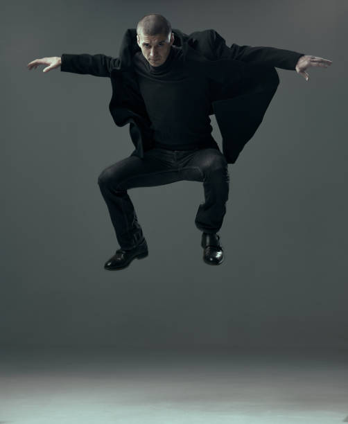istock Jumping cool handsome confident guy in black clothes businessman levitating on gray studio background with copy space. 1298980112